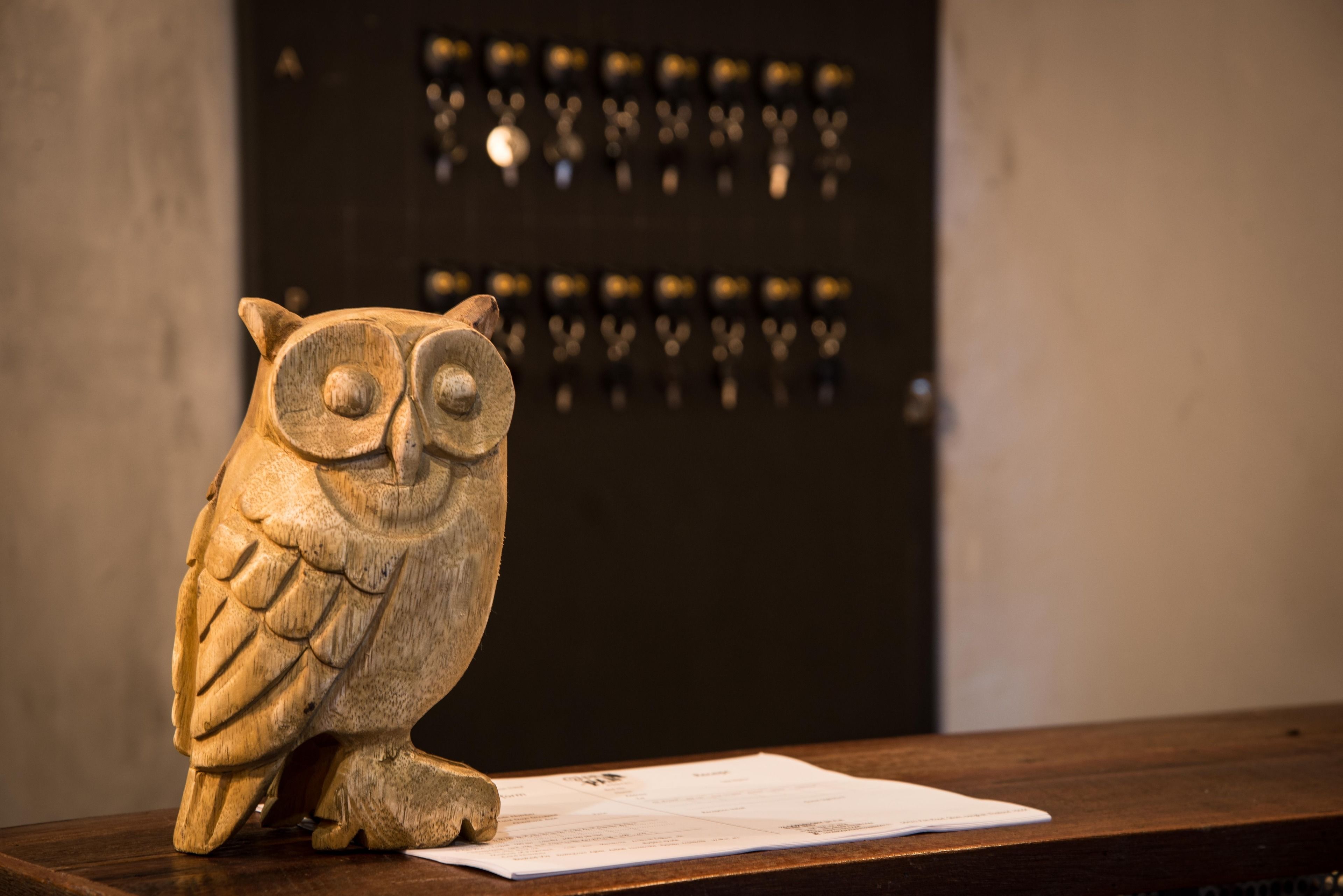 A wooden owl sculpture on a wooden table with papers in front of it.