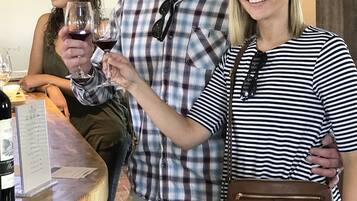 A group of people at a wine tasting event, with a wooden table displaying wine bottles and glasses.