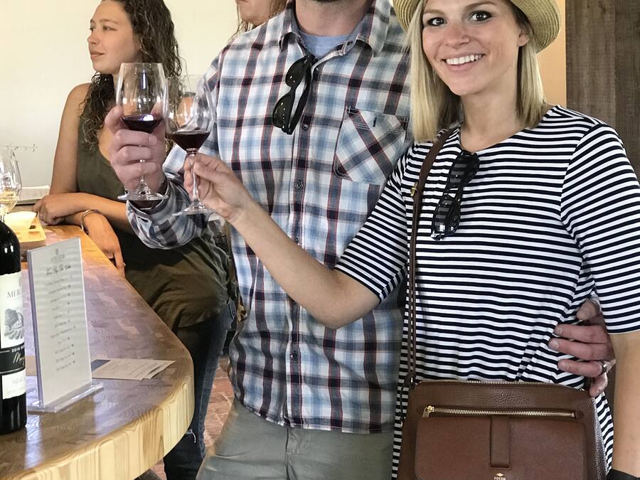 A group of people at a wine tasting event, with a wooden table displaying wine bottles and glasses.