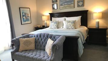 A neatly arranged bedroom with a large bed, two bedside tables with lamps, a tufted armchair, and a framed picture on the wall.
