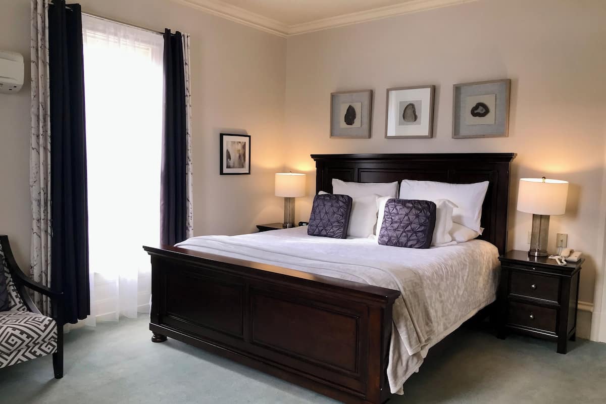 A neatly made bed with a dark wooden headboard, two bedside tables with lamps, and a chair with a patterned seat.