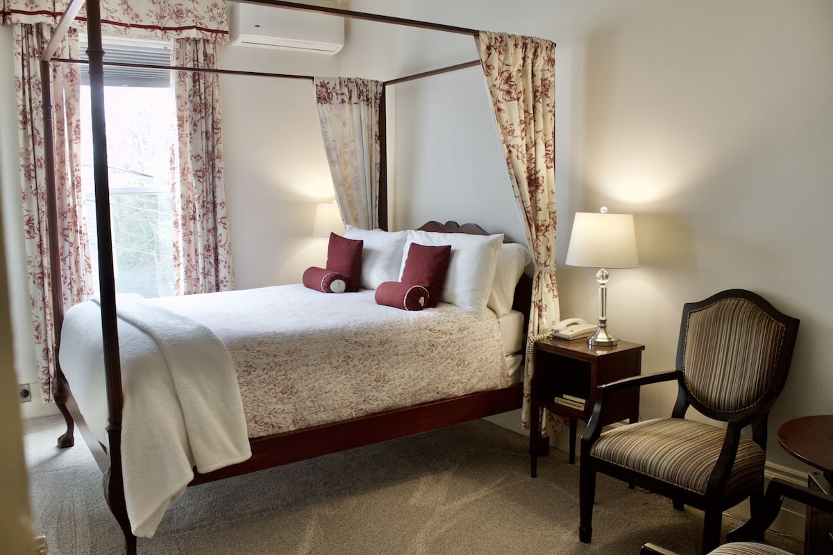 A four-poster bed with a canopy, a bedside table with a lamp, and a chair.