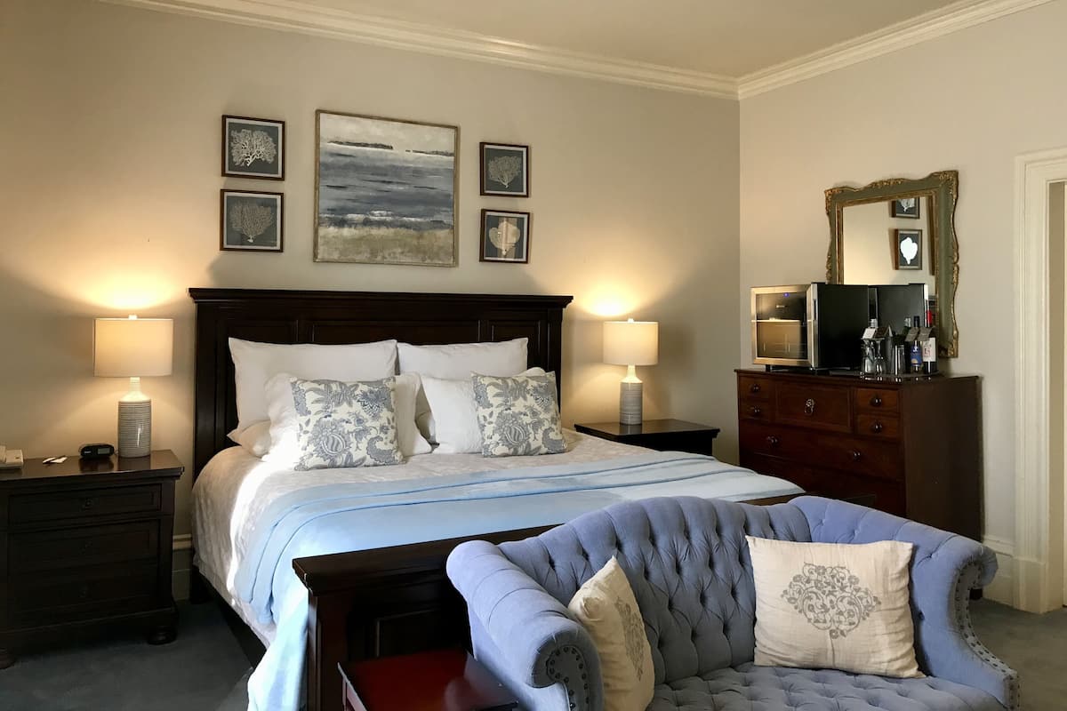 A bedroom with a bed, two bedside tables with lamps, a dresser, a chair, and three framed pictures on the wall.