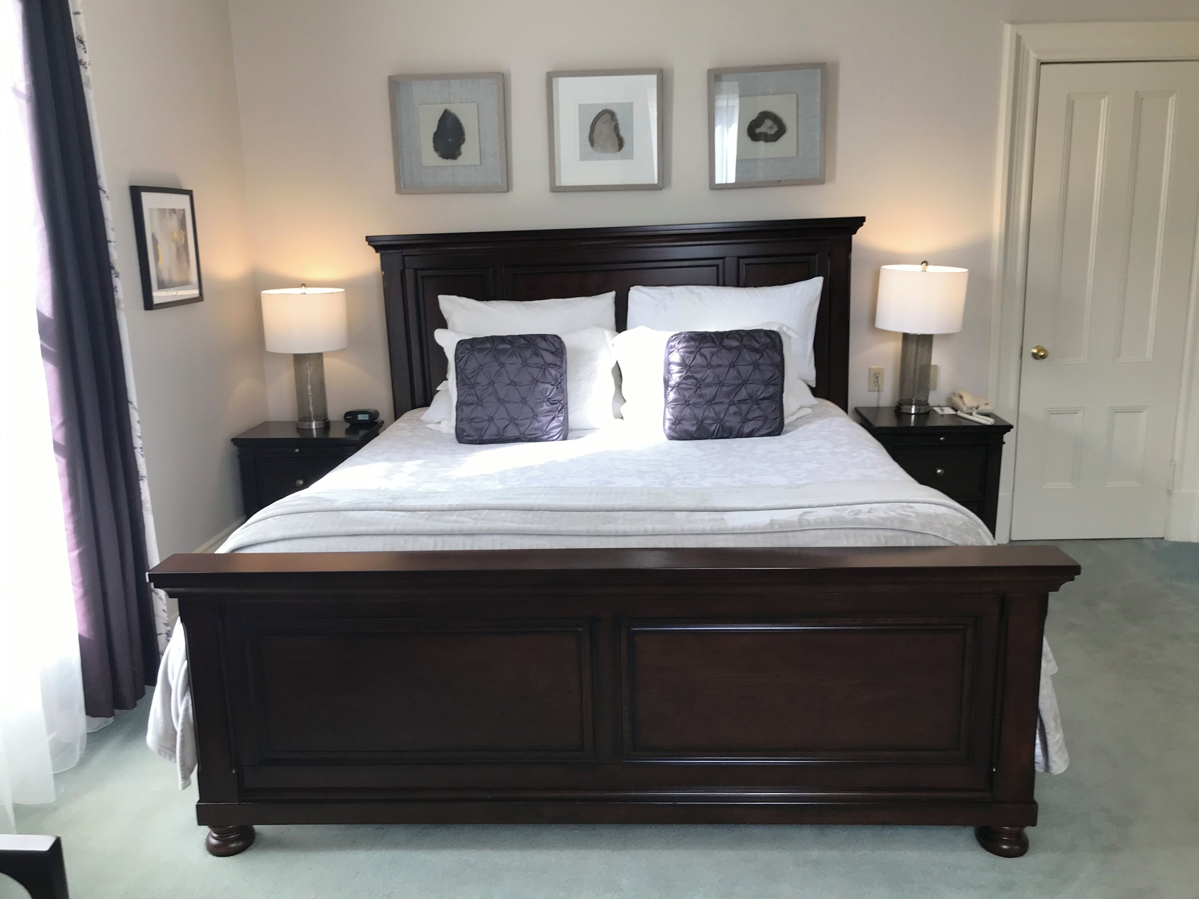 A large bed with a dark headboard, two bedside tables with lamps, and three framed artworks on the wall.