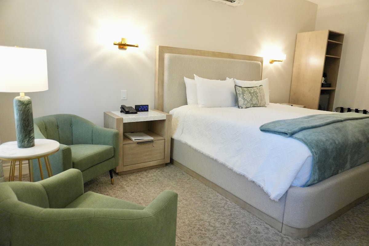 A hotel room with a large bed, a nightstand, a lamp, and a green armchair.