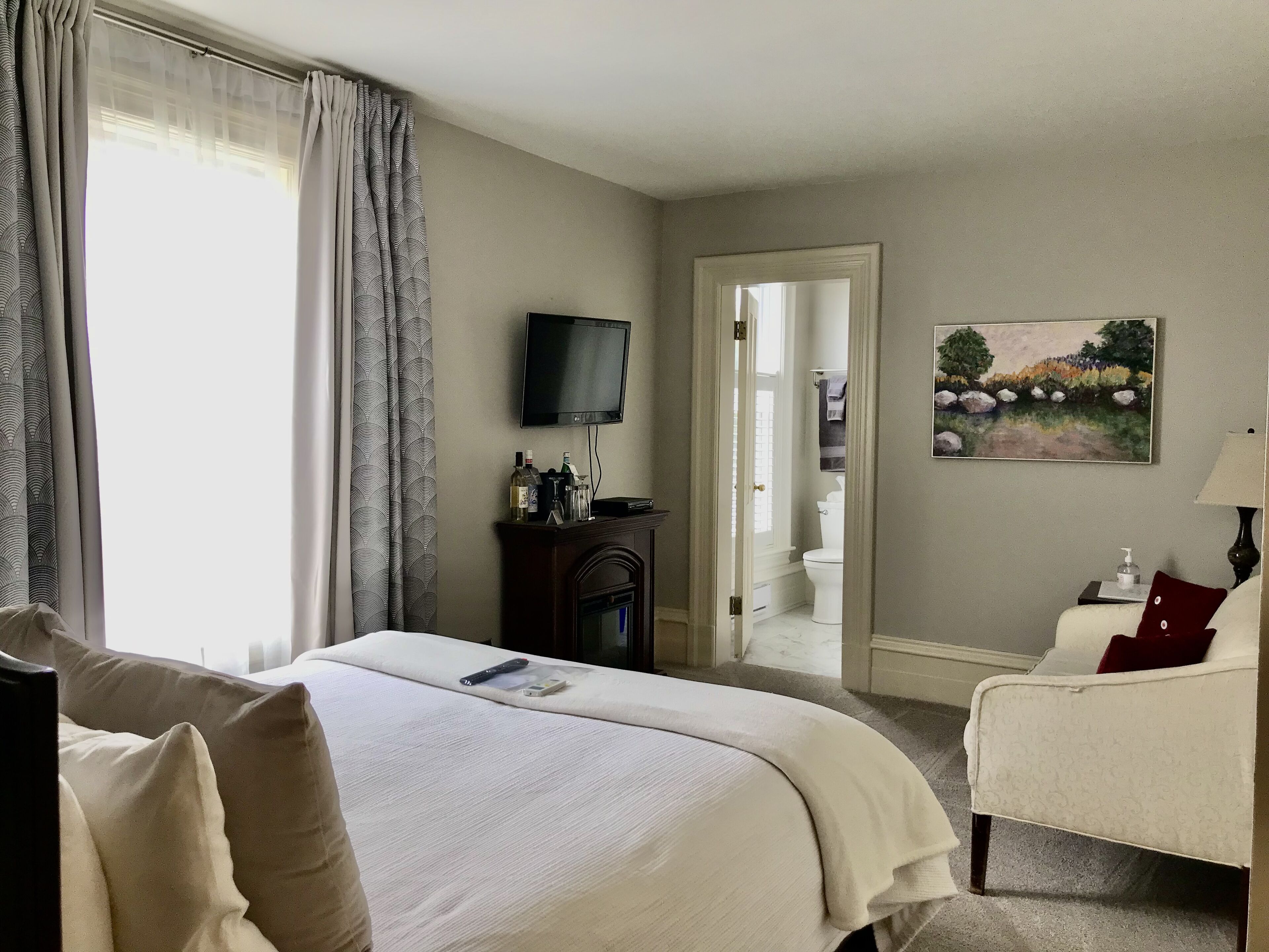 Une chambre d’hôtel avec un lit, une télévision, un tableau et une salle de bain visible à travers une porte ouverte.