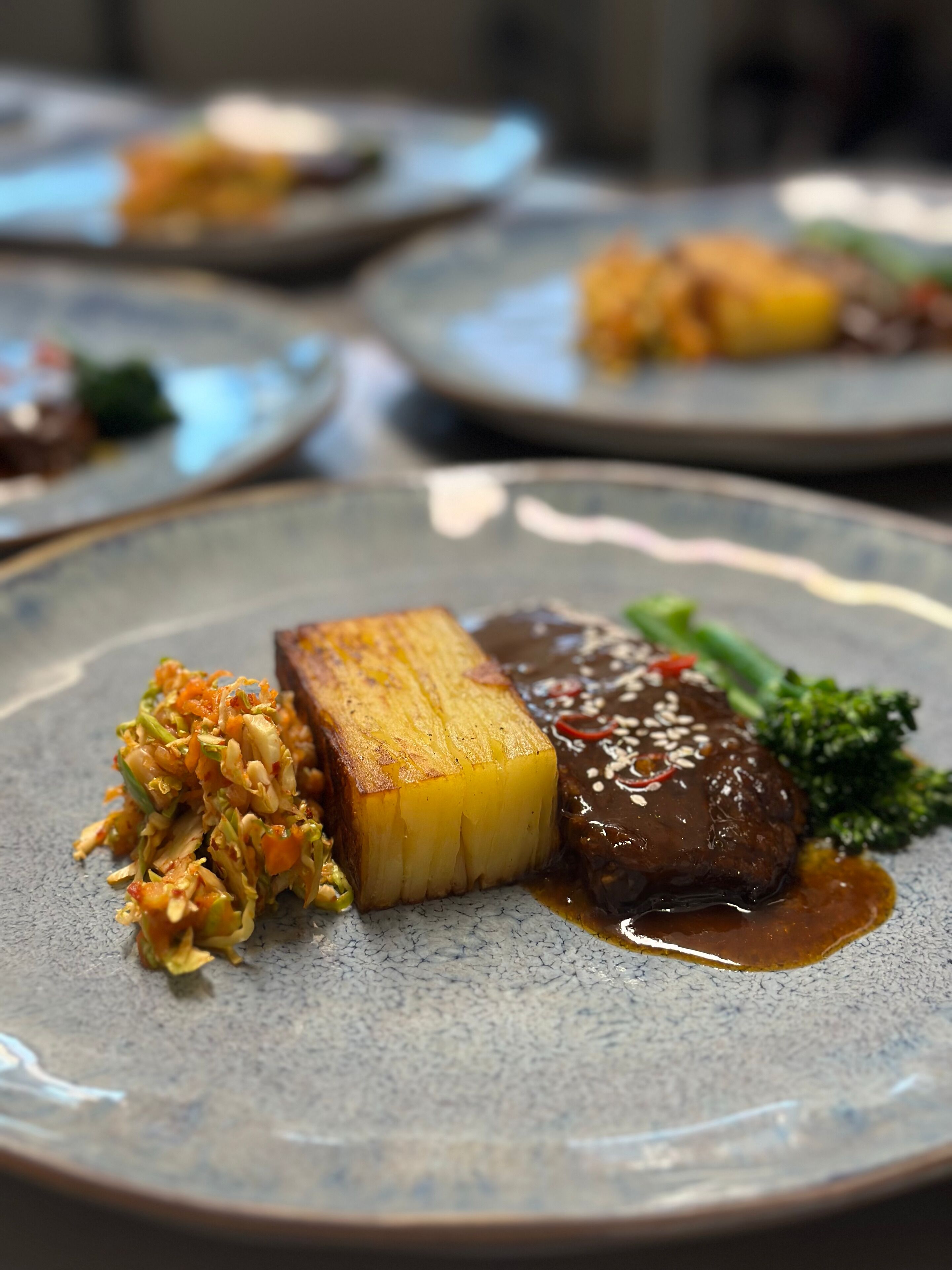 A plate with a piece of meat, a slice of potato, and a side of vegetables.