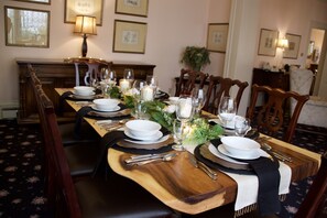 A long dining table set with plates, glasses, and cutlery, surrounded by wooden chairs.