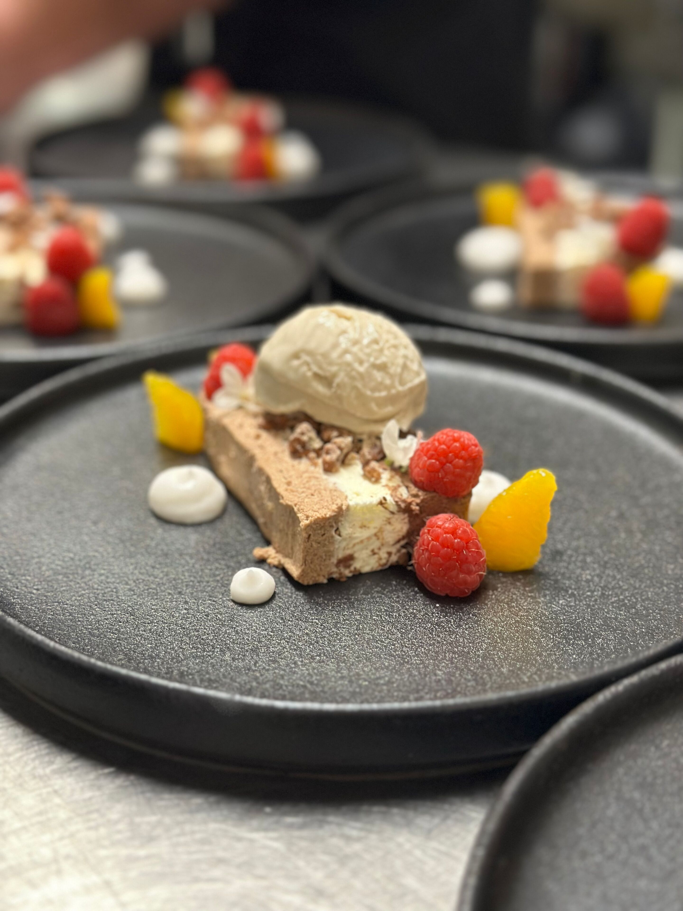 A dessert plate with a scoop of ice cream, chocolate cake, raspberries, and a yellow fruit piece.