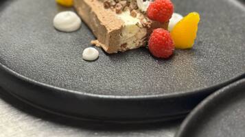 A dessert plate with a scoop of ice cream, chocolate cake, raspberries, and a yellow fruit piece.