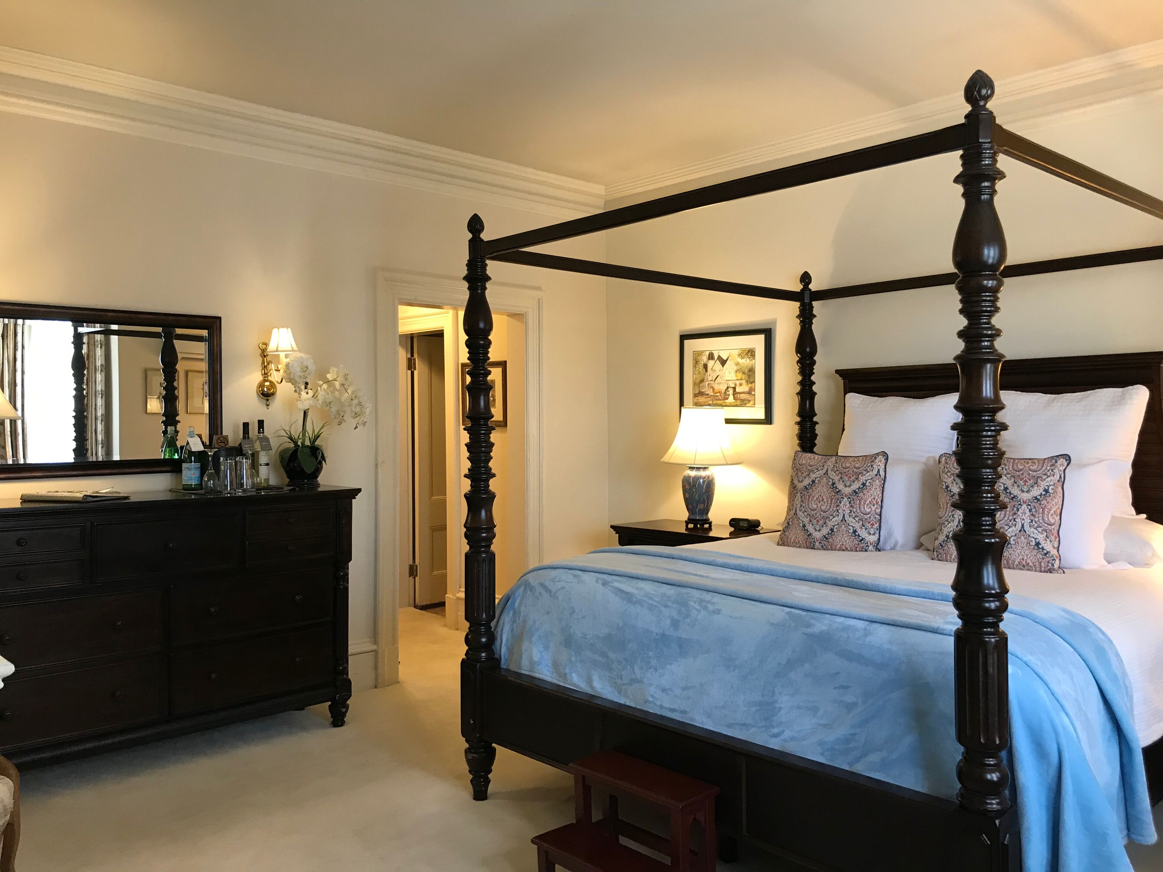 Un lit à baldaquin avec une couvre-lit bleue, une commode avec un miroir et un tableau encadré accroché au mur.