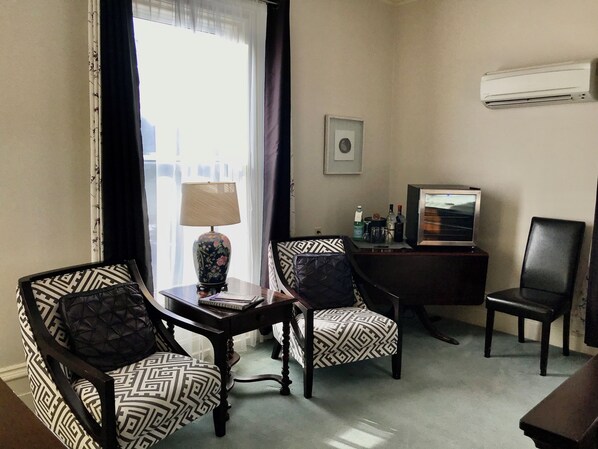 Une chambre d’hôtel avec deux fauteuils à motifs, une petite table avec une lampe, un téléviseur et un tableau au mur.