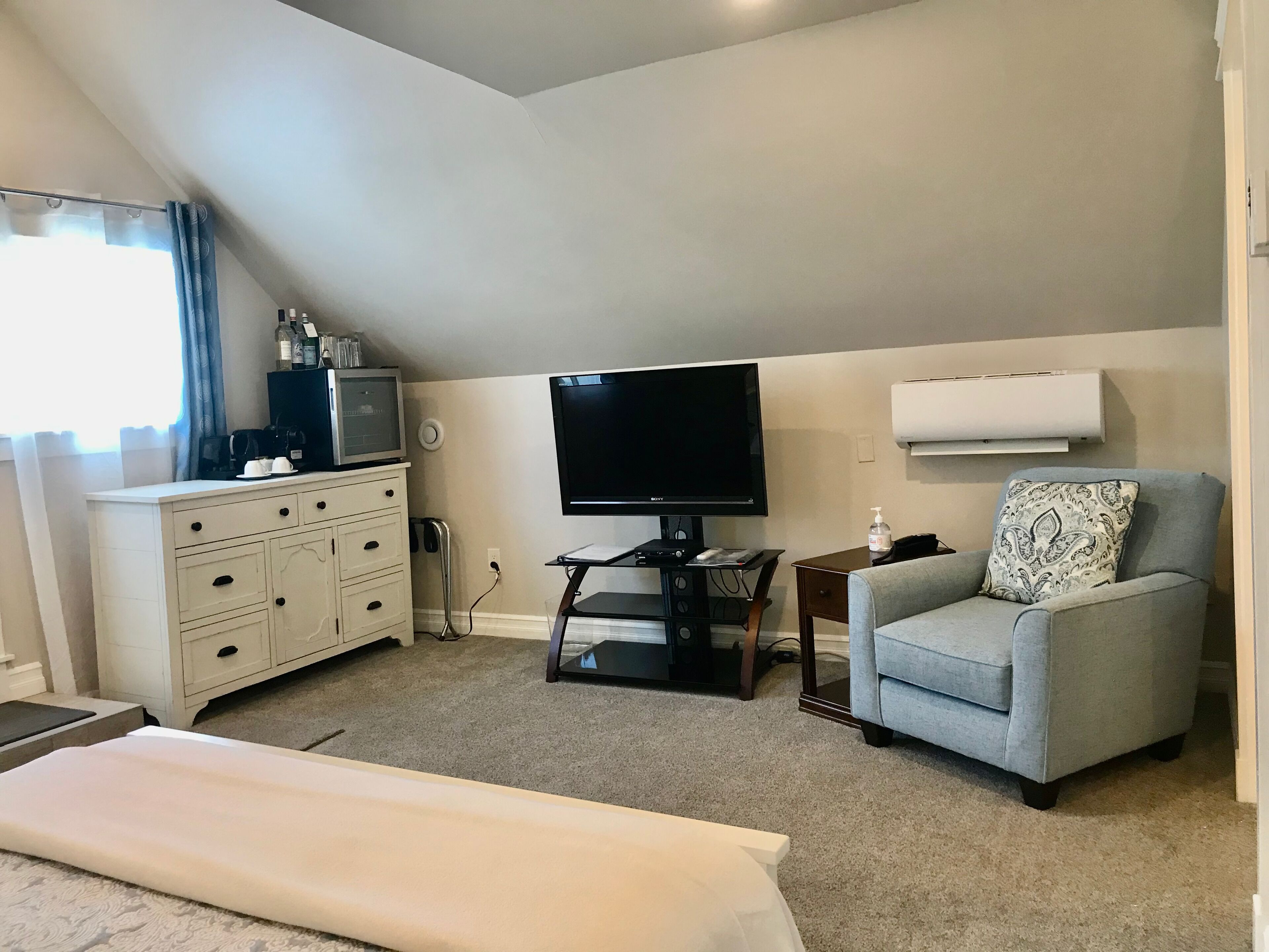 Een hotelkamer met een bed, een televisie, een bureau met een computer, een stoel, een dressoir en een raam met gordijnen.