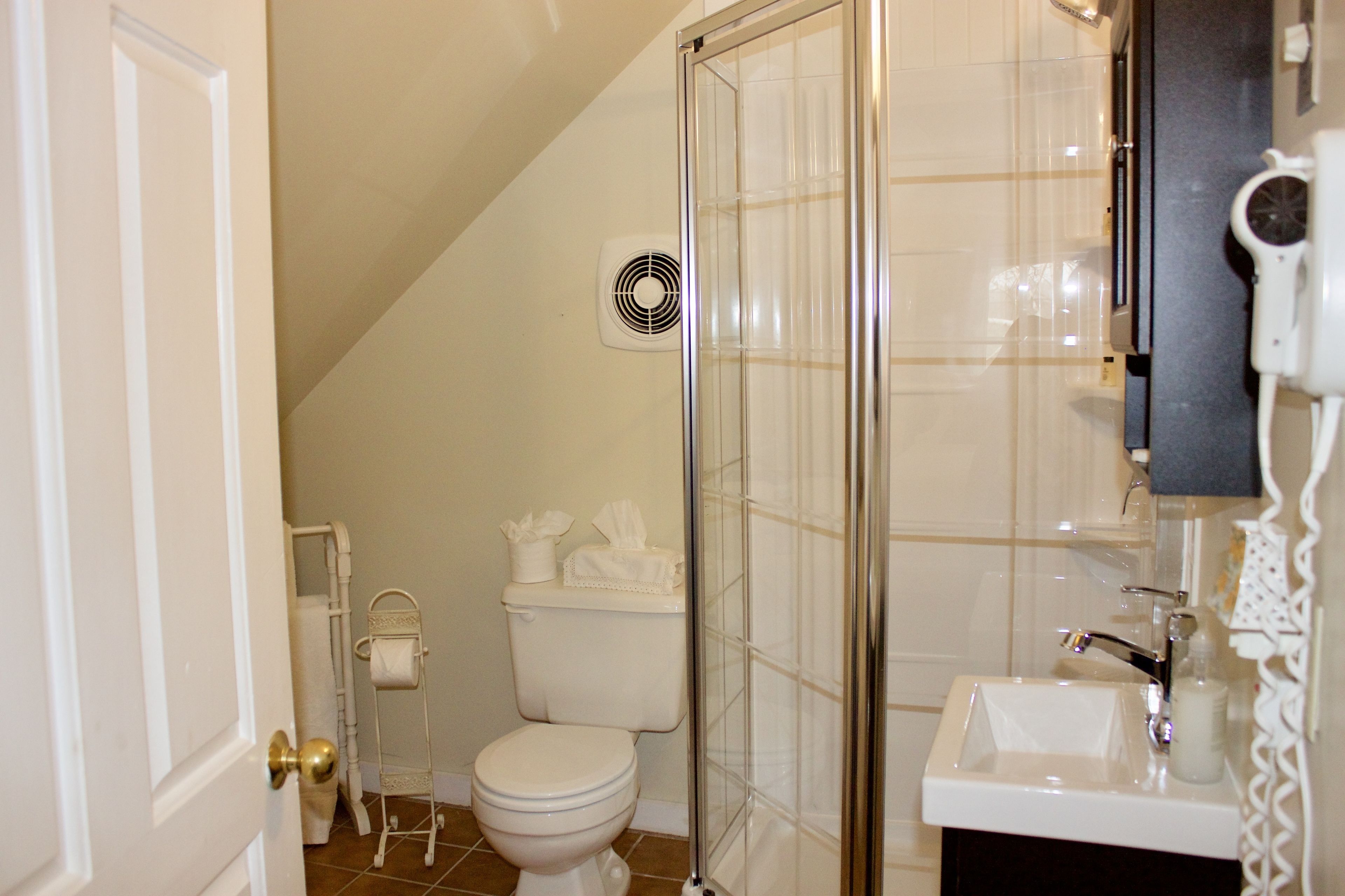 Un baño con inodoro, cabina de ducha de vidrio, lavamanos y secador de pelo.