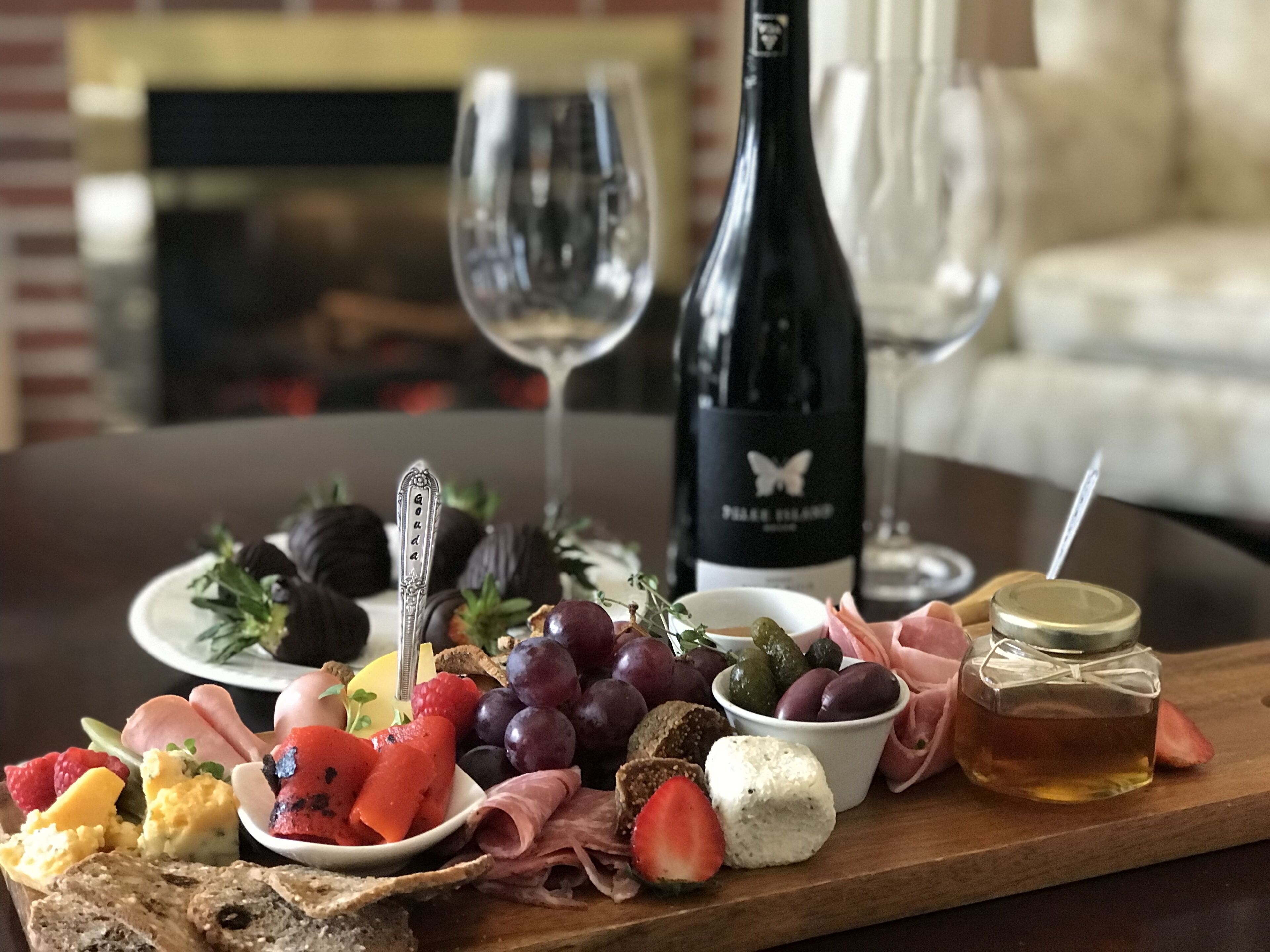 A charcuterie board with various cheeses, fruits, and meats, accompanied by wine glasses and a bottle of wine.