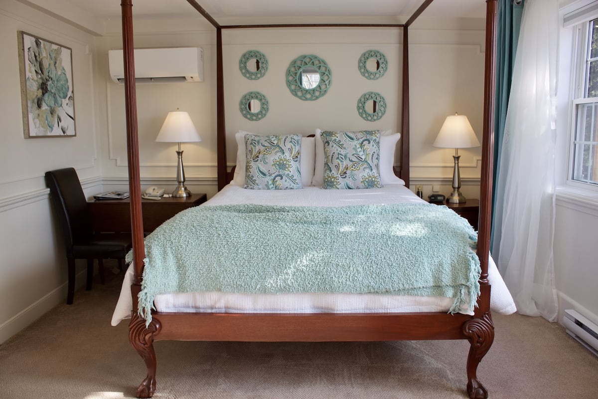A four-poster bed with a green blanket, two bedside lamps, and decorative wall mirrors.