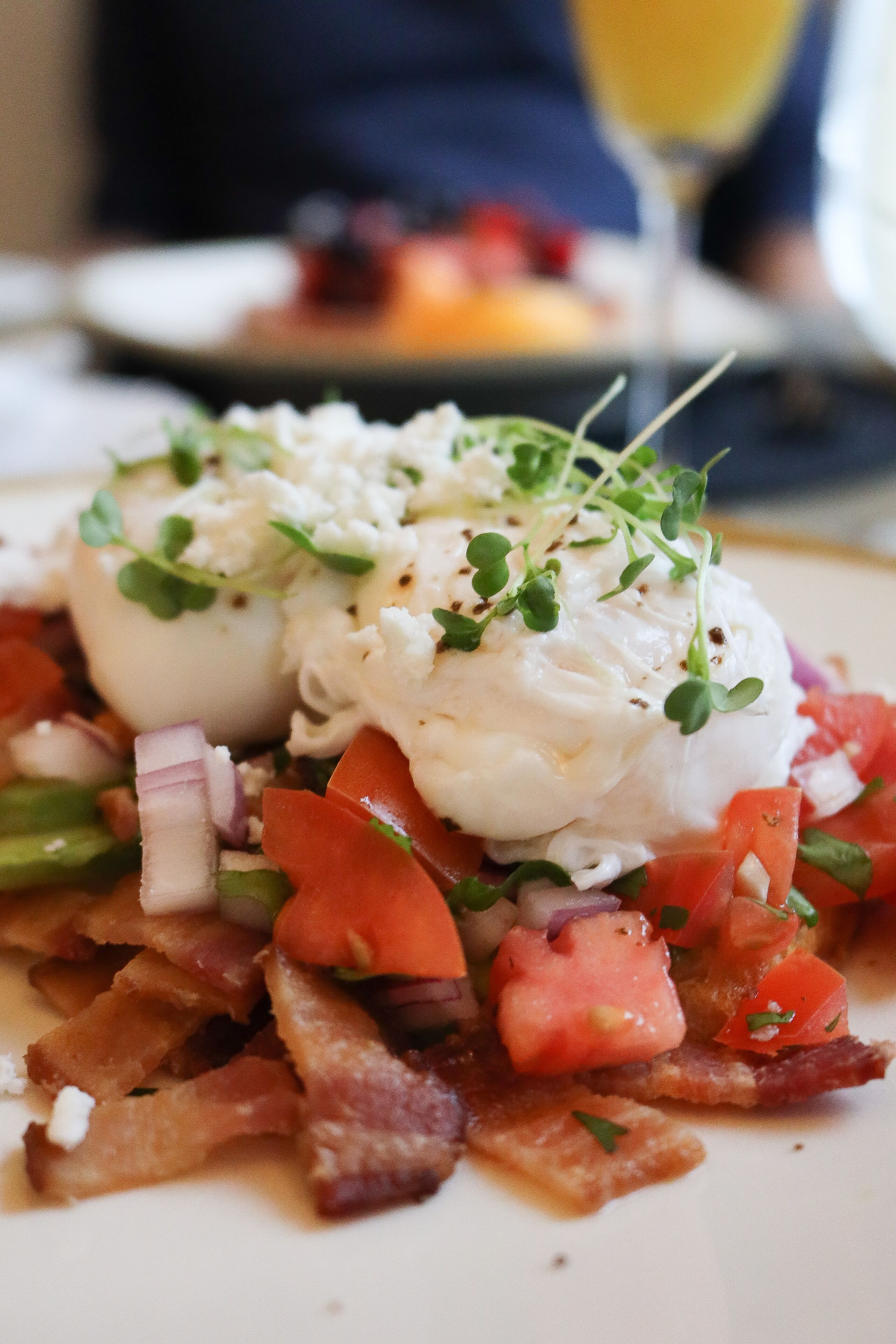 Un plato de desayuno con huevos pochados, tocino, tomates y vegetales verdes.