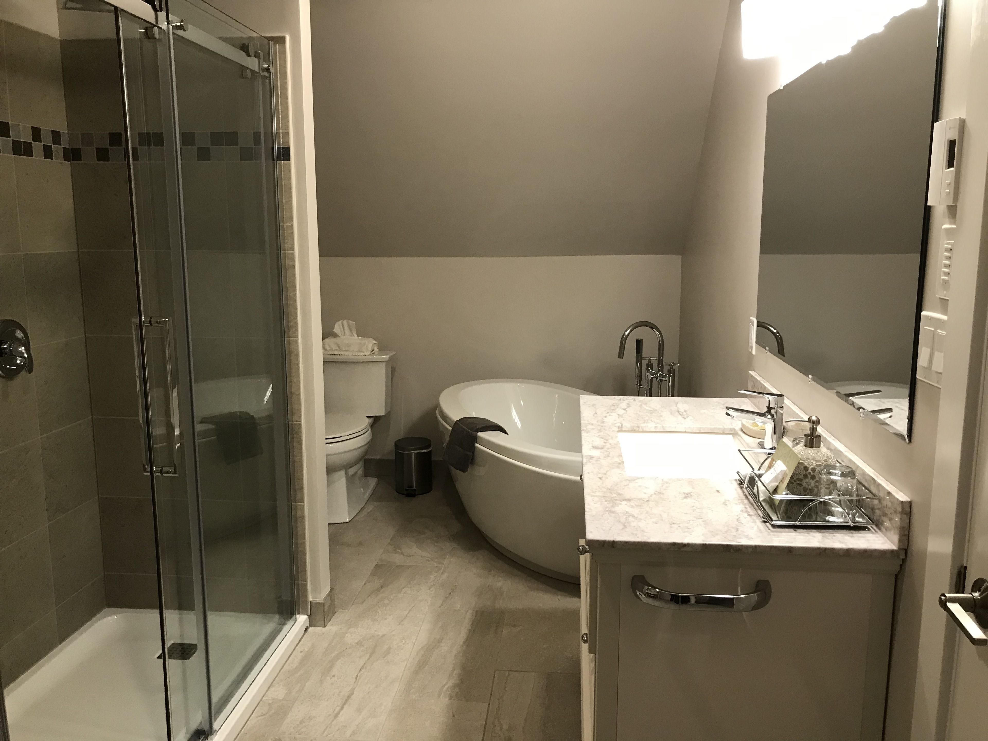 A bathroom with a glass-enclosed shower, a toilet, a bathtub, and a sink with a mirror.