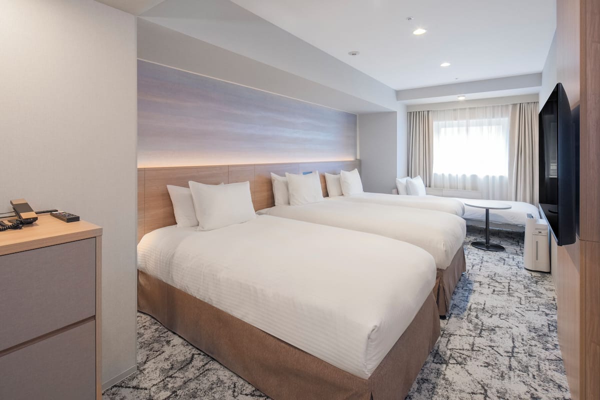 Une chambre d’hôtel avec deux lits, un bureau, une télévision et une grande fenêtre avec des rideaux.