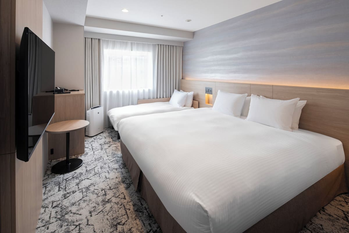 Une chambre d’hôtel avec deux lits, un téléviseur à écran plat, une petite table et une grande fenêtre avec des rideaux.