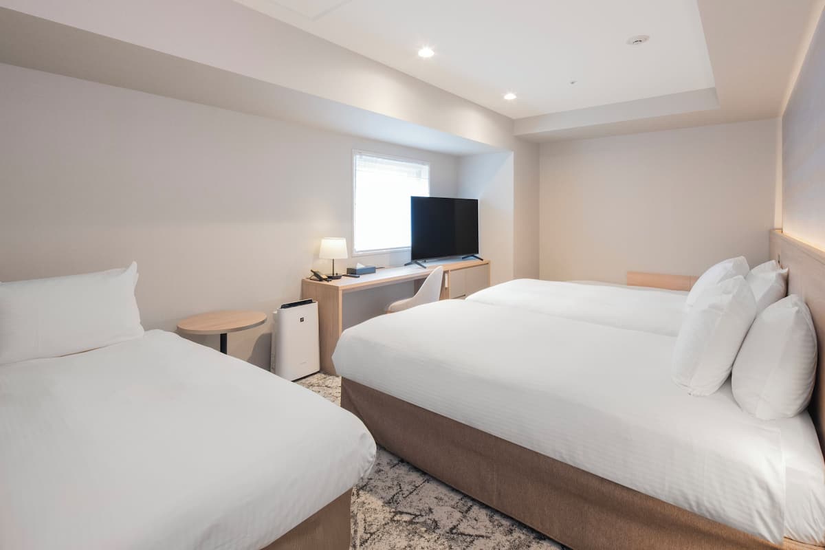 Une chambre d’hôtel avec deux lits, un bureau avec une télévision et une fenêtre.