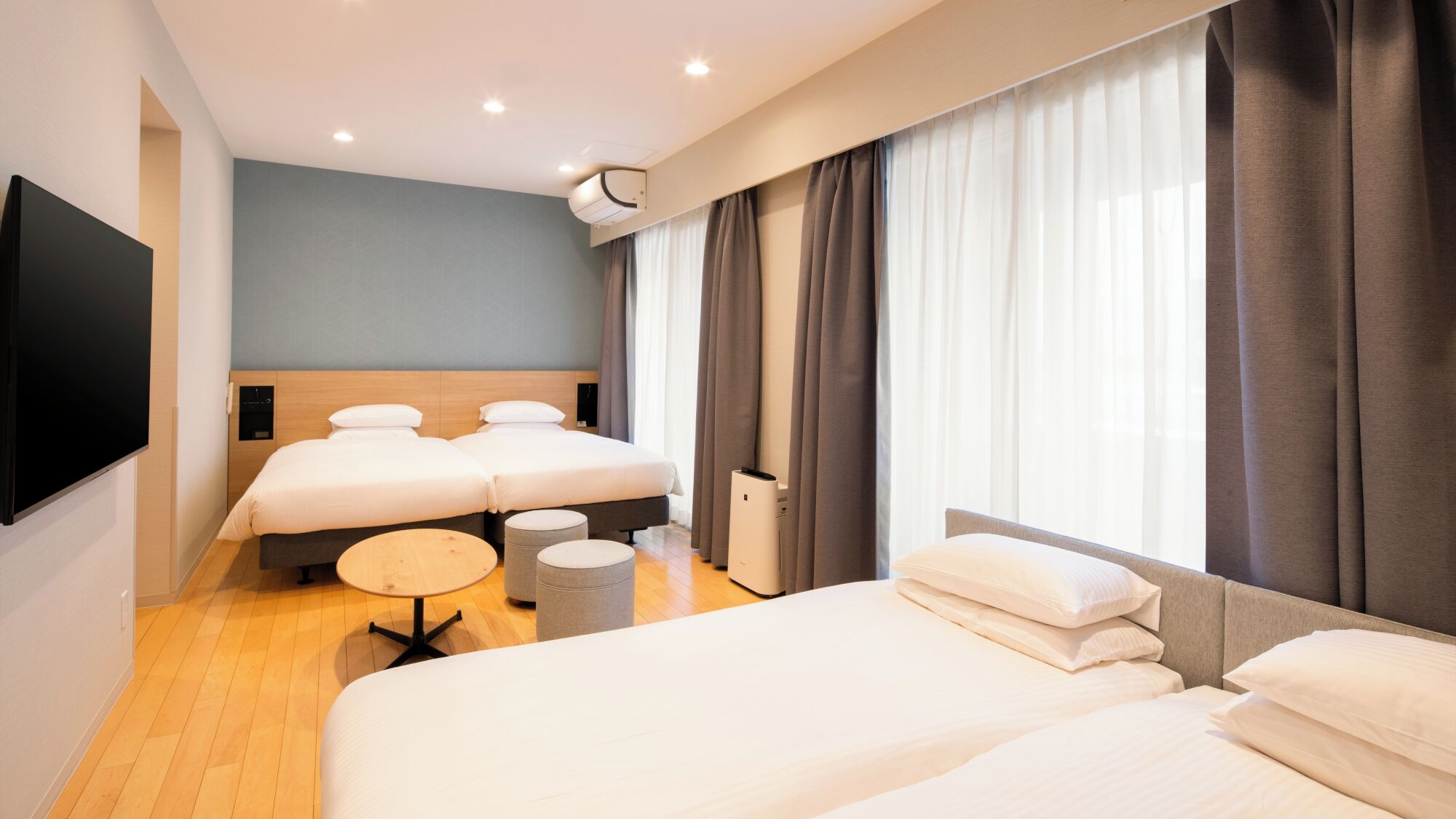 Une chambre d’hôtel avec deux lits, une télévision, une machine à café et une grande fenêtre avec des rideaux.