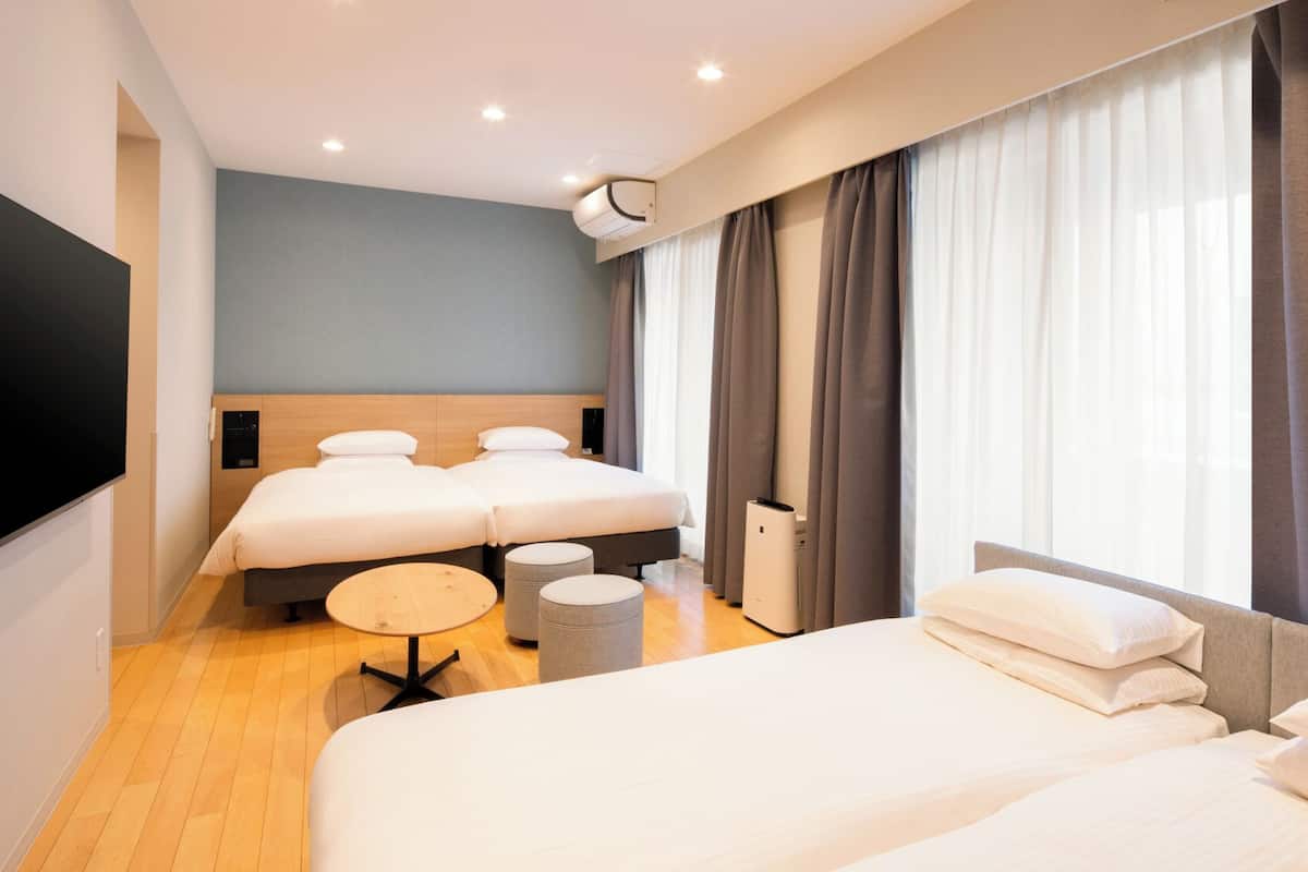 Een hotelkamer met twee bedden, een televisie, een koffieapparaat en een groot raam met gordijnen.