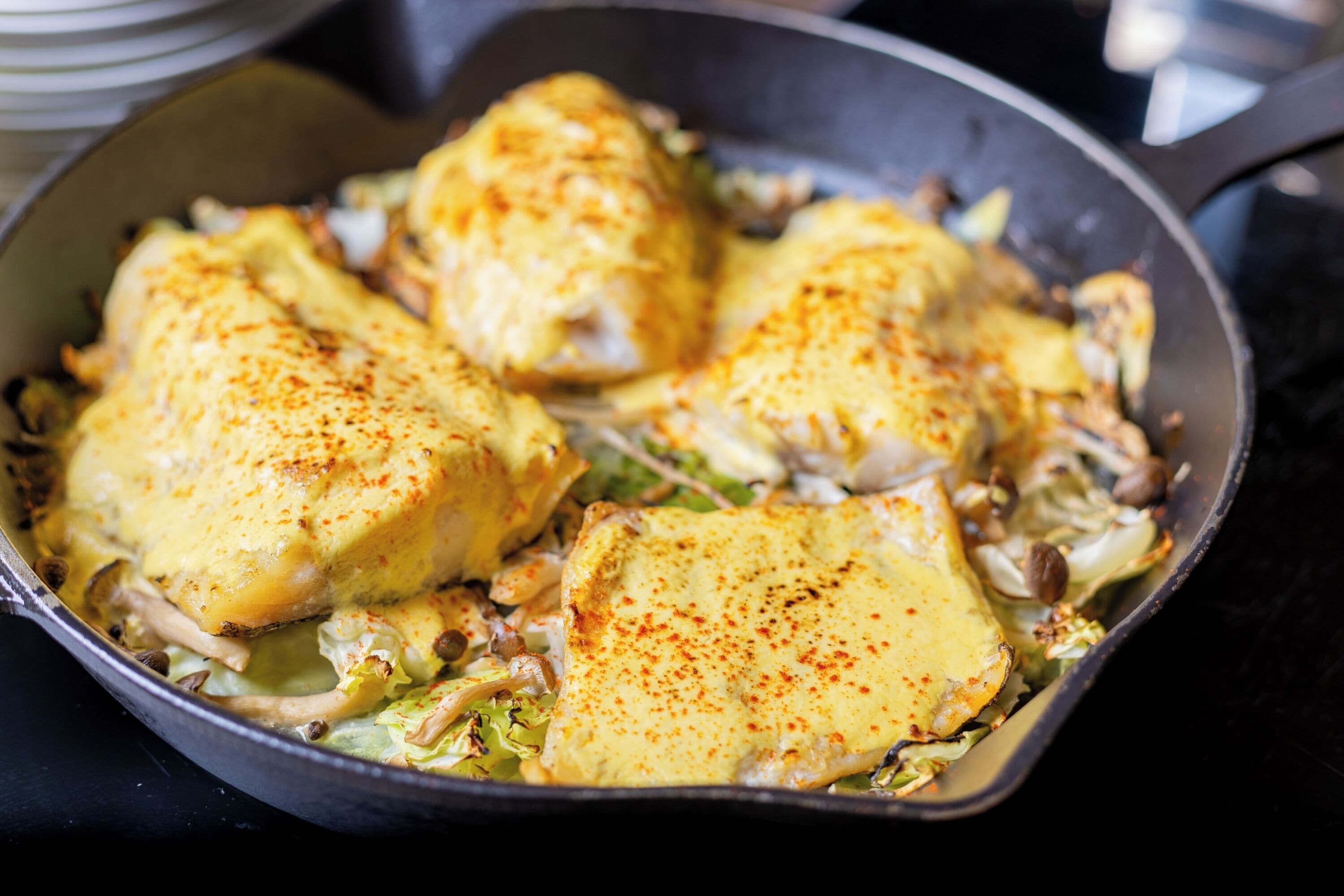 Een koekenpan met kippefilets, bedekt met kaas en kruiden.