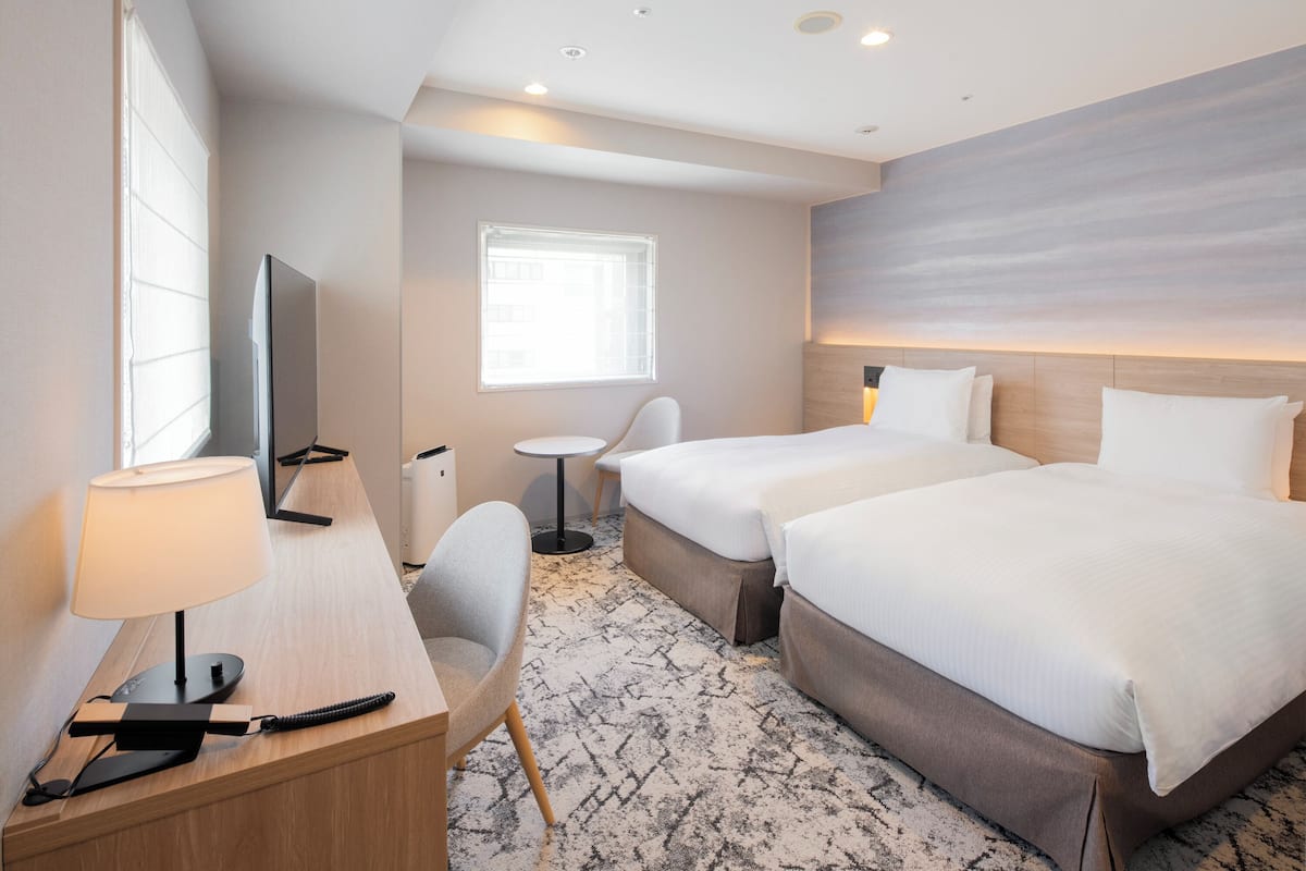 Une chambre d’hôtel avec deux lits, un bureau avec une lampe, une chaise, une télévision et une petite table.