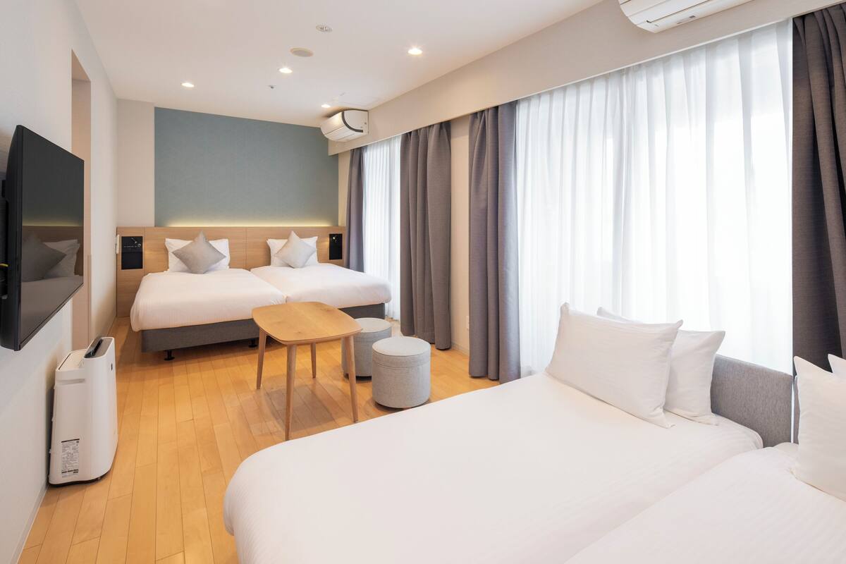 Une chambre d’hôtel avec deux lits, une télévision, une petite table et une poubelle.