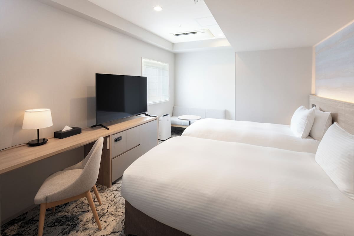 Une chambre d’hôtel comprenant un lit, un bureau avec une chaise, une télévision et une fenêtre.