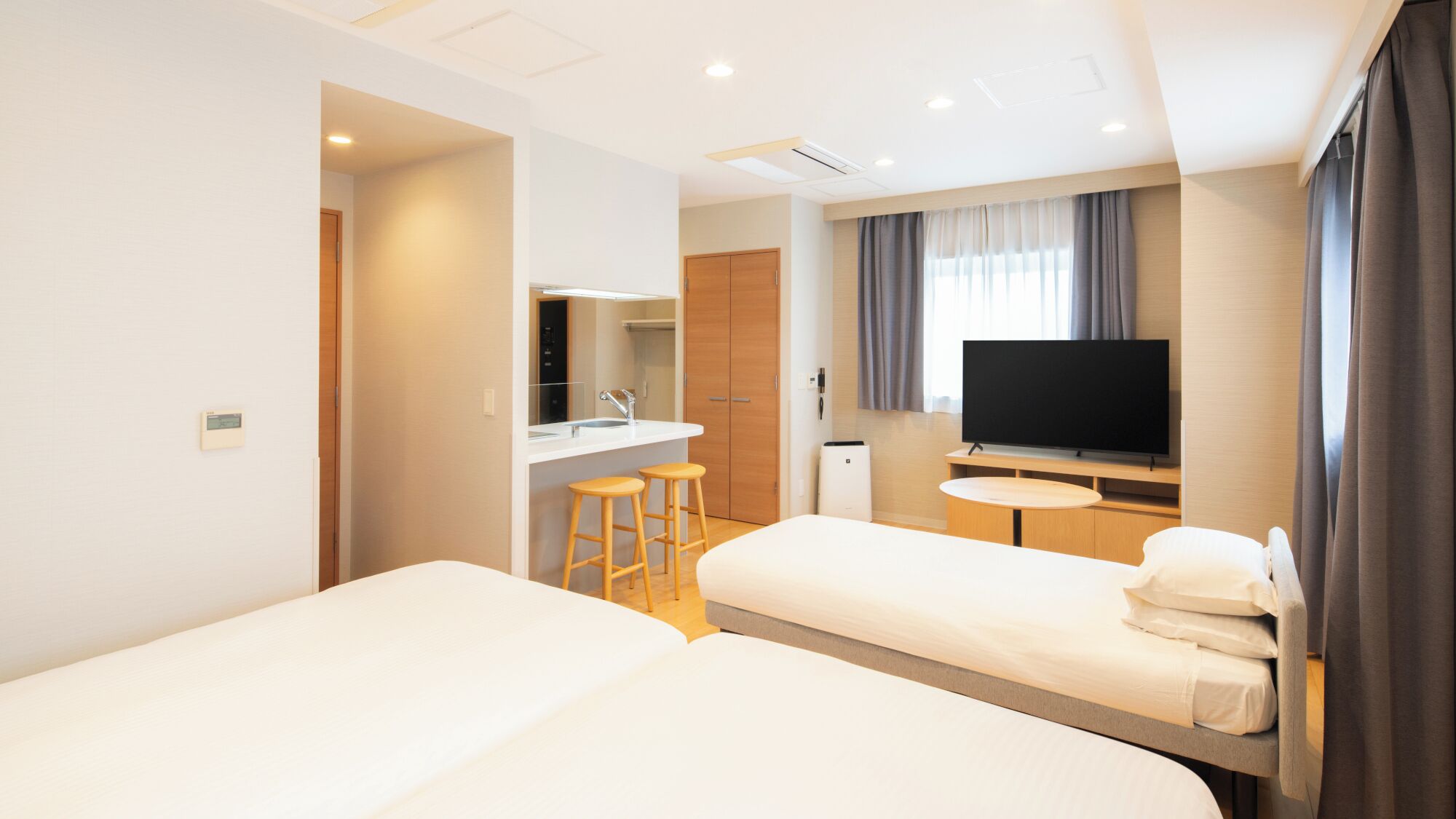 Une chambre d’hôtel avec deux lits, une télévision, une petite table, un miroir et une salle de bain avec un lavabo et des toilettes.