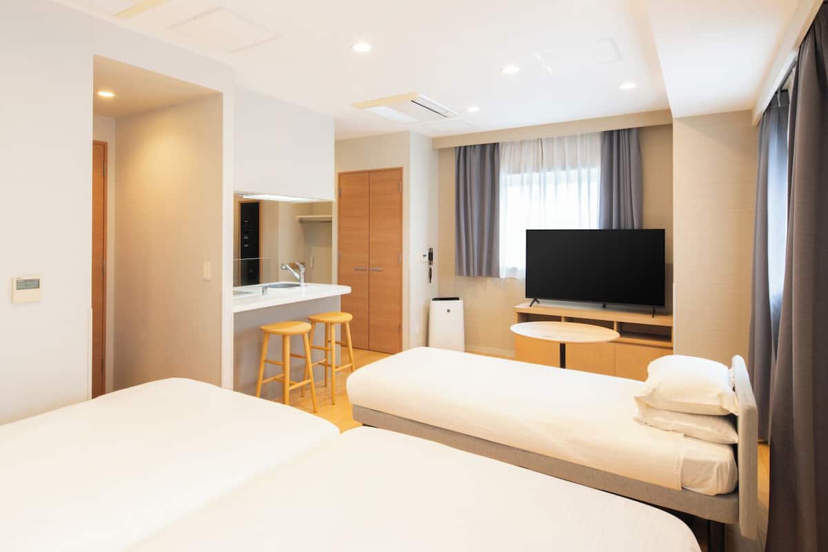 Hotelkamer met twee bedden, een televisie, een klein tafeltje, een spiegel en een badkamer met wastafel en toilet.