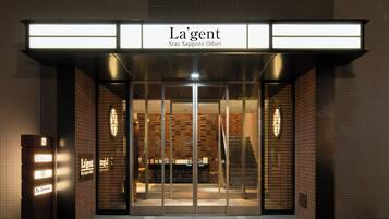 The entrance of La'gent hotel with a modern design, featuring a glass door and illuminated signage.