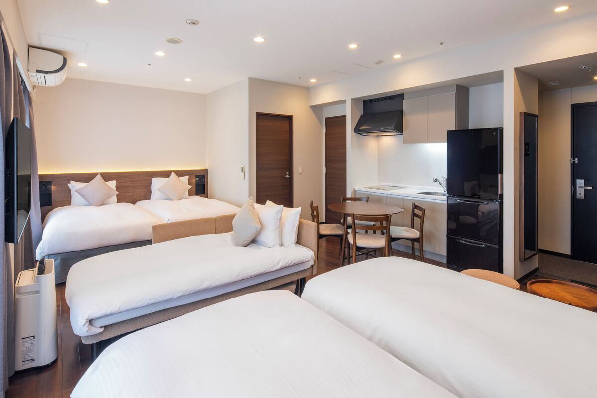 Une chambre d’hôtel avec trois lits, une kitchenette et un coin repas.