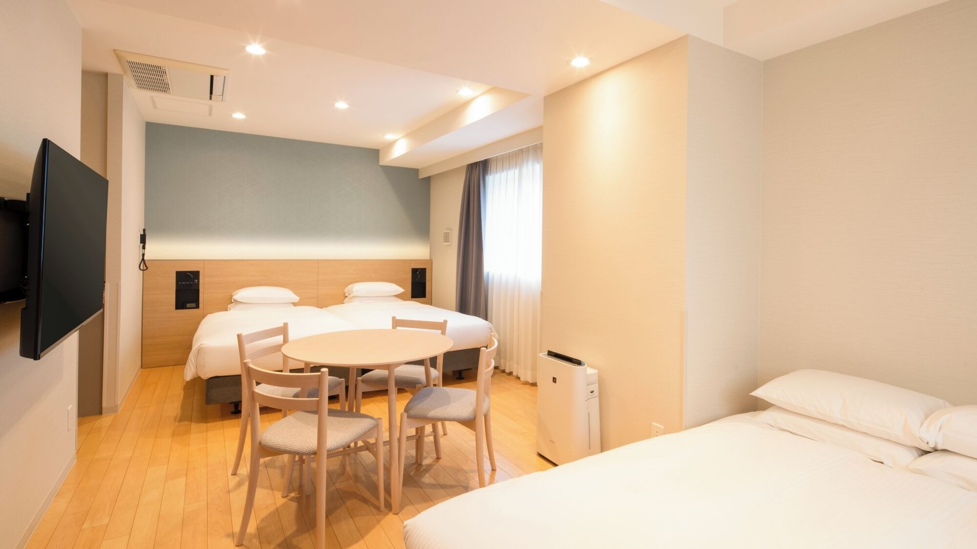 Une chambre d’hôtel avec un lit, un bureau, deux chaises, une télévision et une fenêtre avec des rideaux.