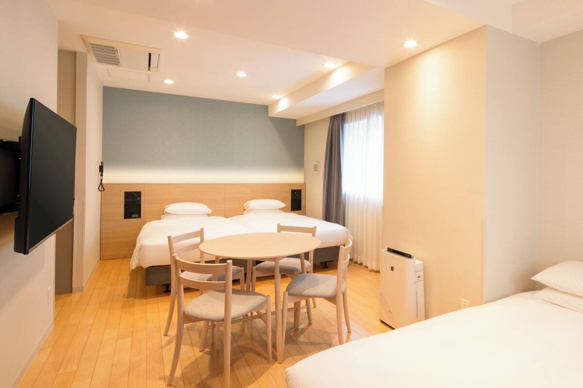 Een hotelkamer met een bed, een bureau, twee stoelen, een televisie en een raam met gordijnen.