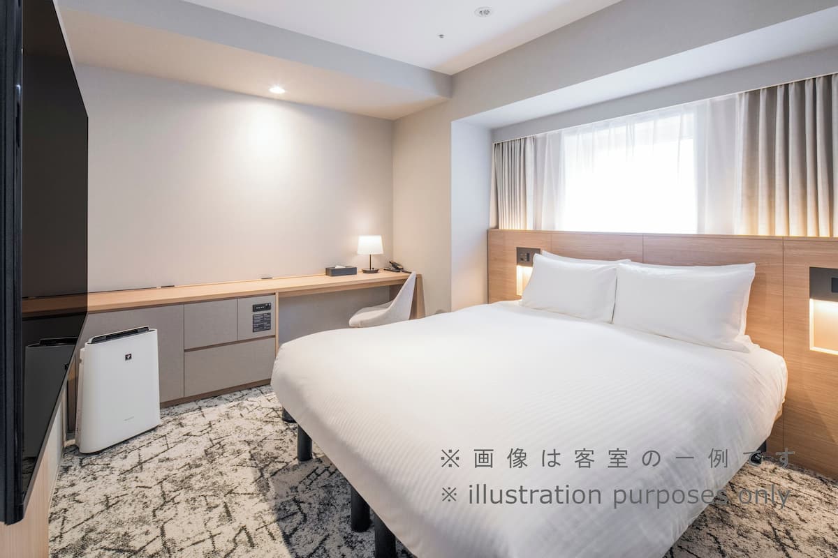Une chambre d’hôtel comprenant un lit, une table de chevet, une lampe et un petit bureau avec une chaise.