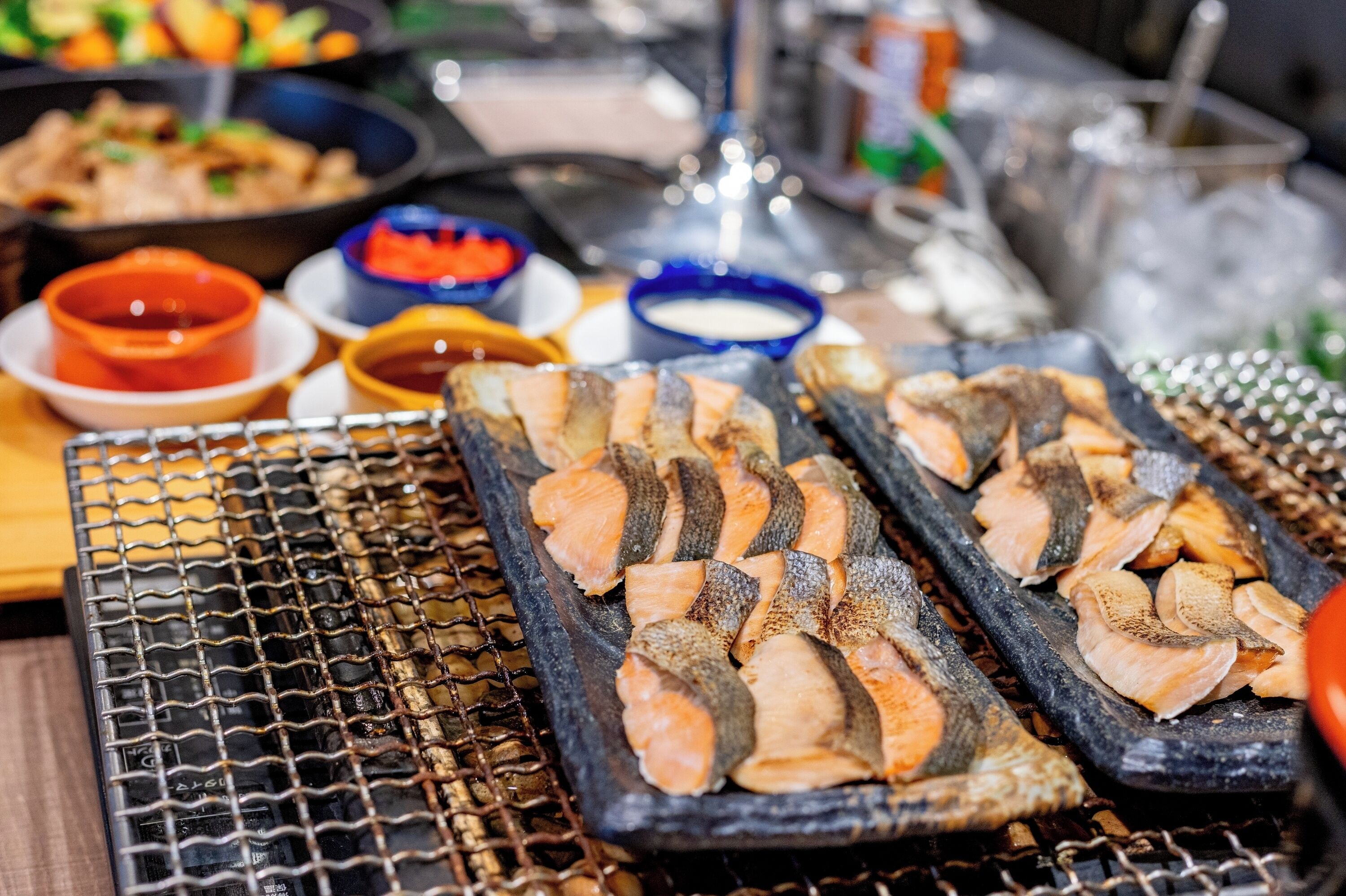 Grilled salmon on a grill with various dipping sauces in the background.