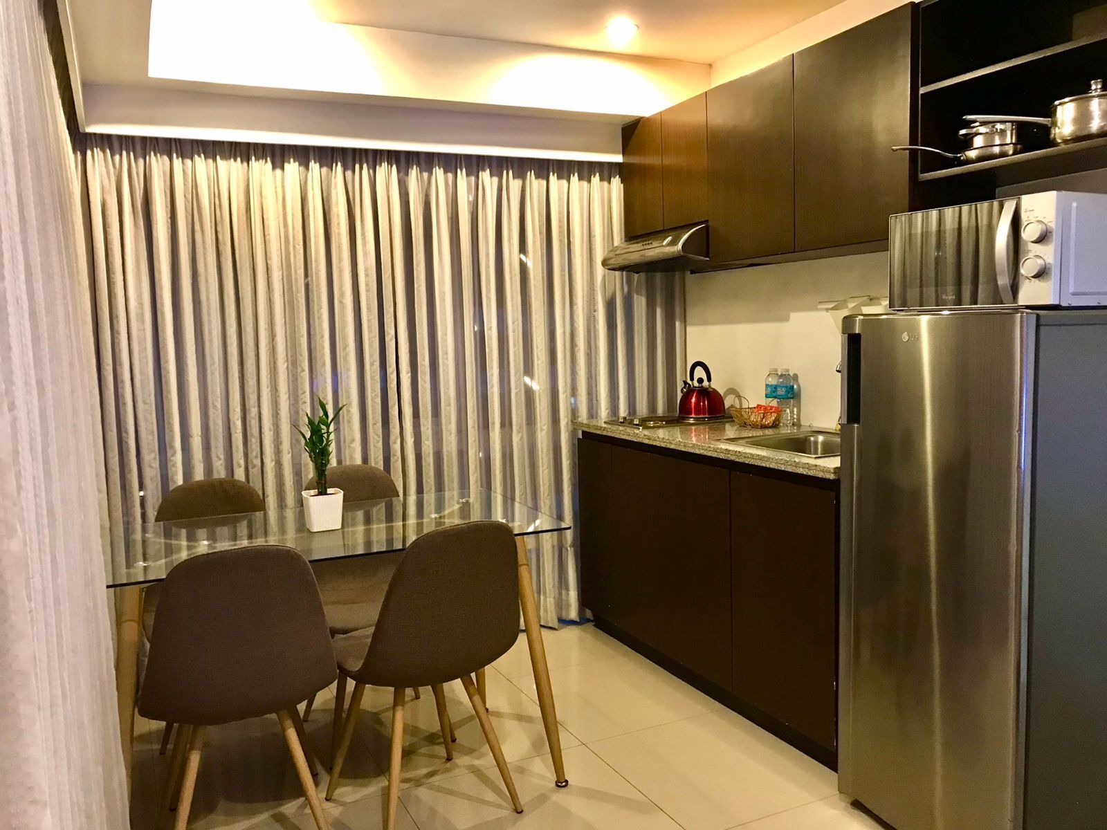 A modern kitchen with a refrigerator, kettle, and a glass table with chairs.