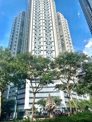 A tall residential building with multiple balconies, surrounded by trees and a central sculpture. - MaxStays Max Style at Fort Victoria (Taguig)