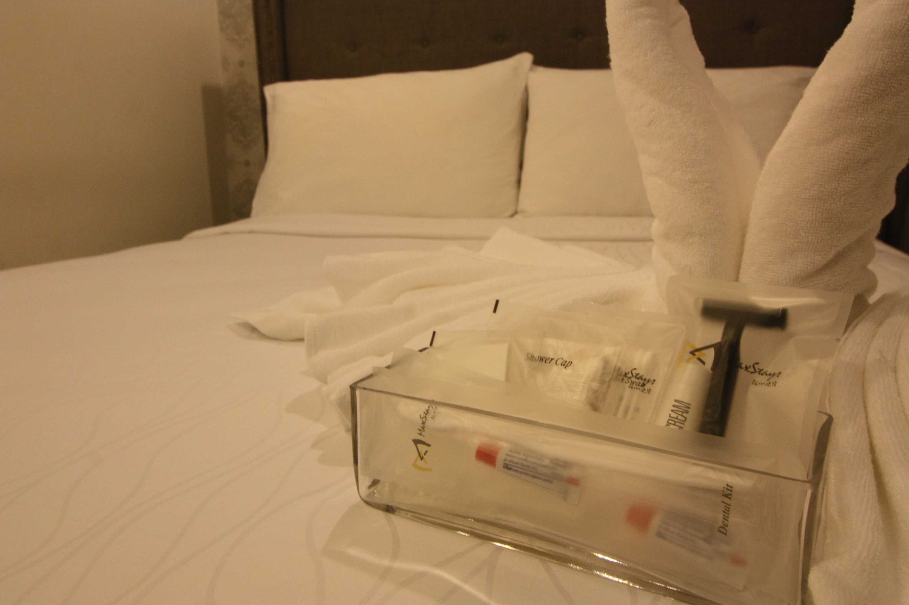 Un récipient transparent en verre contenant des articles de toilette, posé sur une table de chevet recouverte de linge de lit blanc.