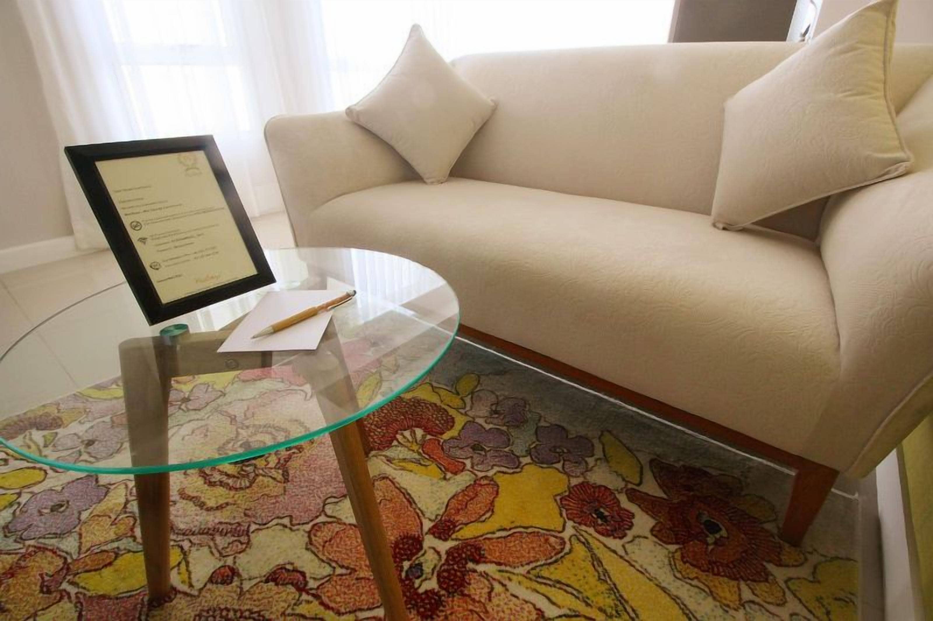 Una habitación con una mesa de vidrio, un menú enmarcado, un sofá y una alfombra con estampado floral.