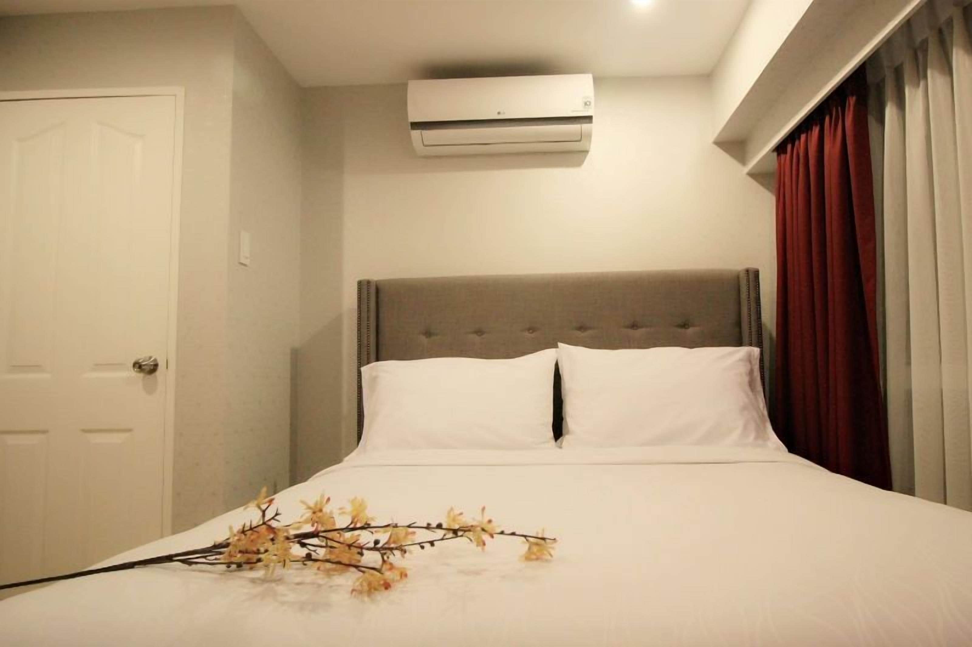 A hotel room with a bed, a door, an air conditioning unit, and a window with curtains.