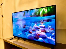 Un televisor de pantalla plana sobre un pedestal, mostrando una escena con conchas marinas y velas.