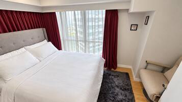 A bedroom with a large bed, a chair, a window with curtains, and a small rug.