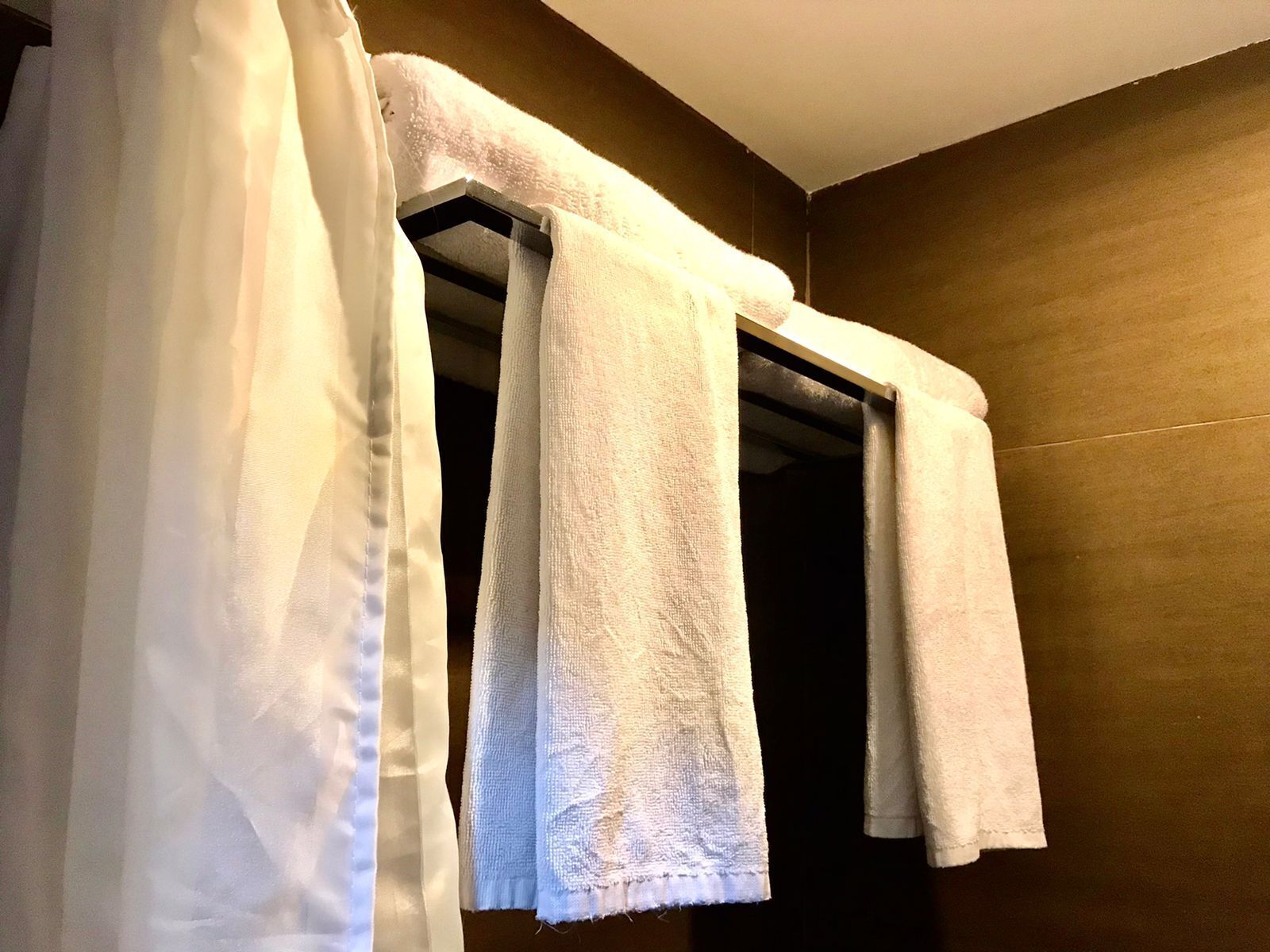A bathroom with a shower curtain, a towel rack with three towels, and a wooden wall.
