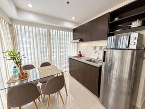 A modern kitchen with a stainless steel refrigerator, a built-in oven, and a microwave. There is a dining table with chairs and a potted plant. - MaxStays Max Style at Fort Victoria (Taguig)