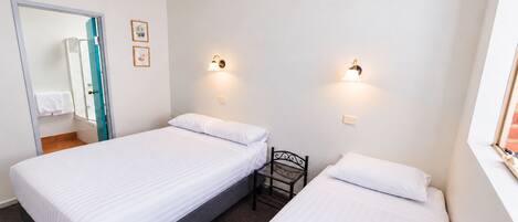 A hotel room with two single beds, a small chair, a mirror, and two wall-mounted lights.
