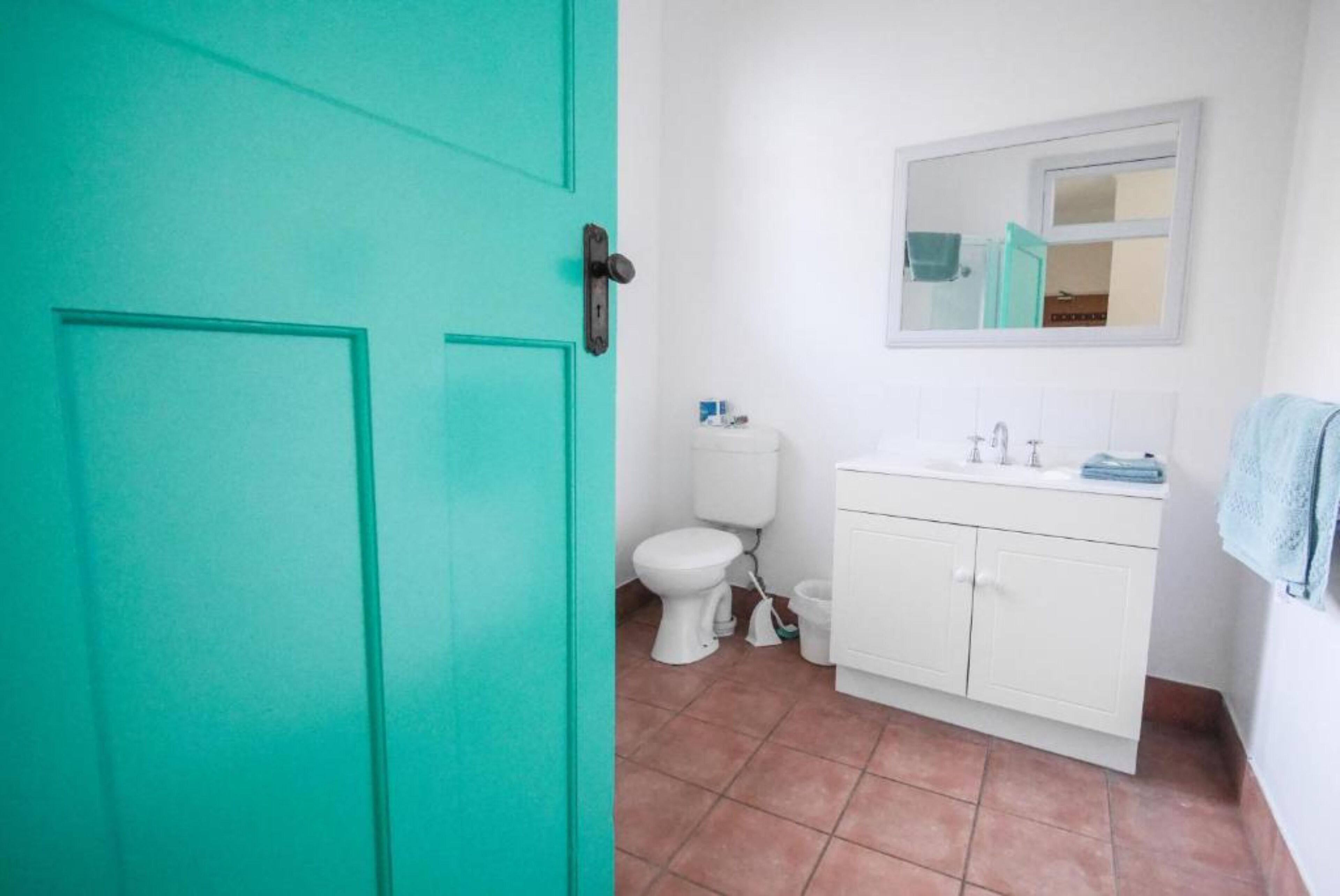 Uma casa de banho com sanita branca, lavatório branco e espelho sobre o lavatório.